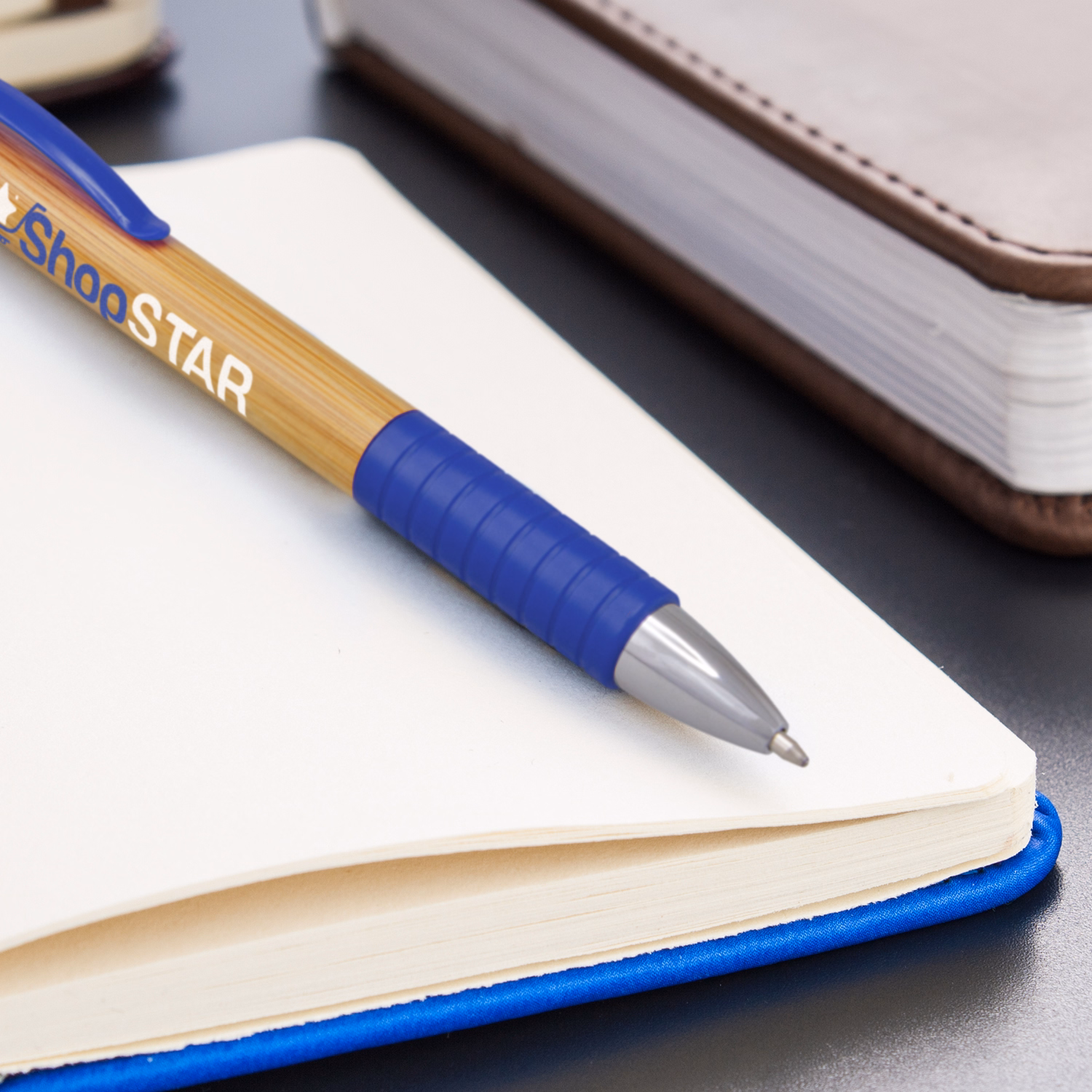 Branded bamboo barrel pen with blue rubber grip and silver tip on notebook
