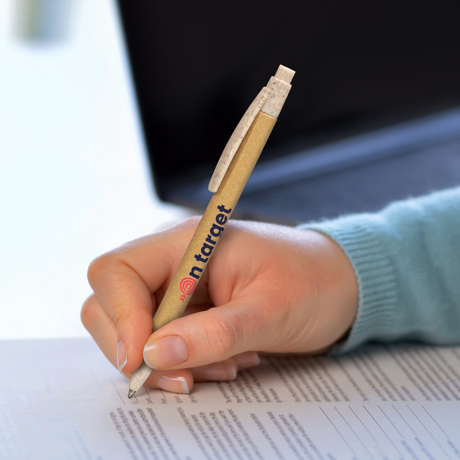 Hand holding branded natural cardboard barrel pen with speckled clip, writing on form