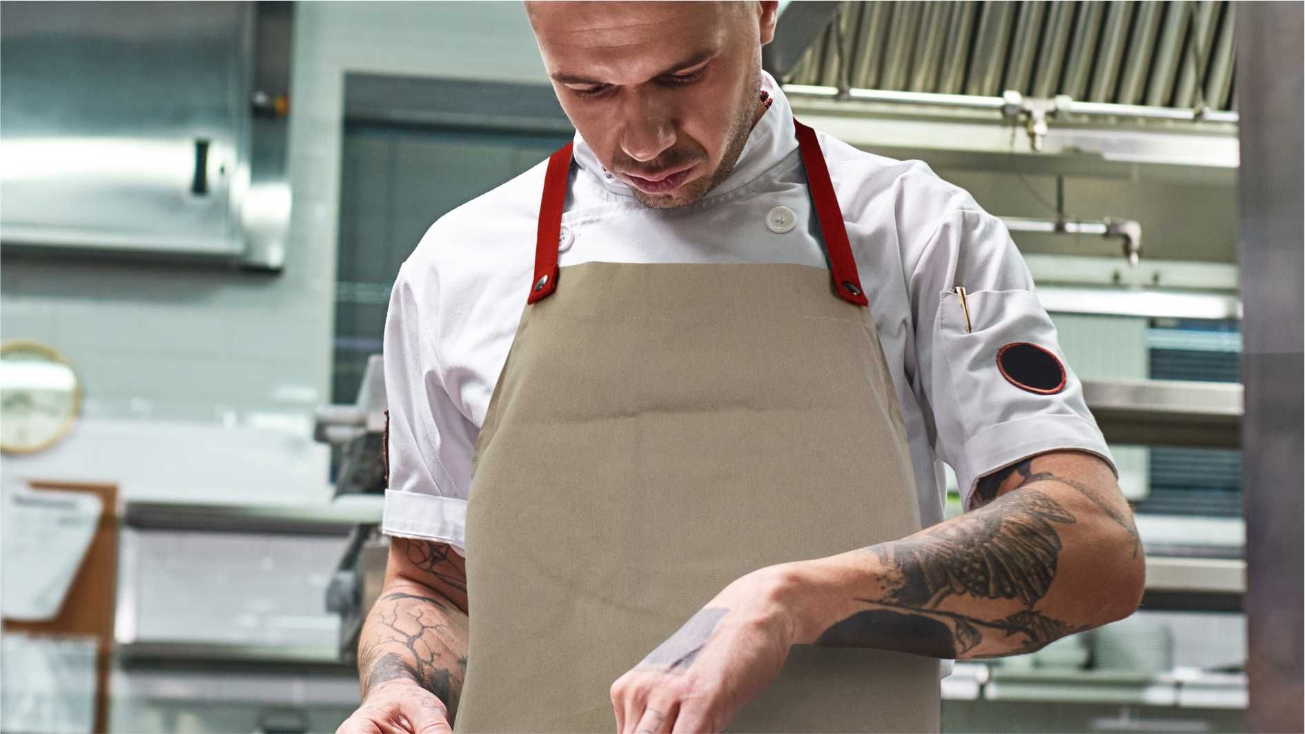 Chef wearing beige apron with red straps while preparing food in kitchen.