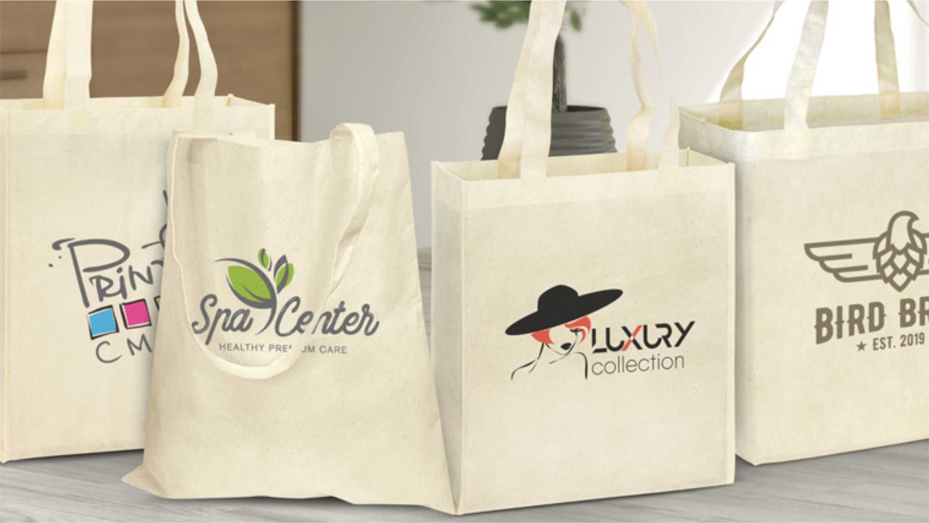 Reusable natural cotton tote bags with printed business logos on table.