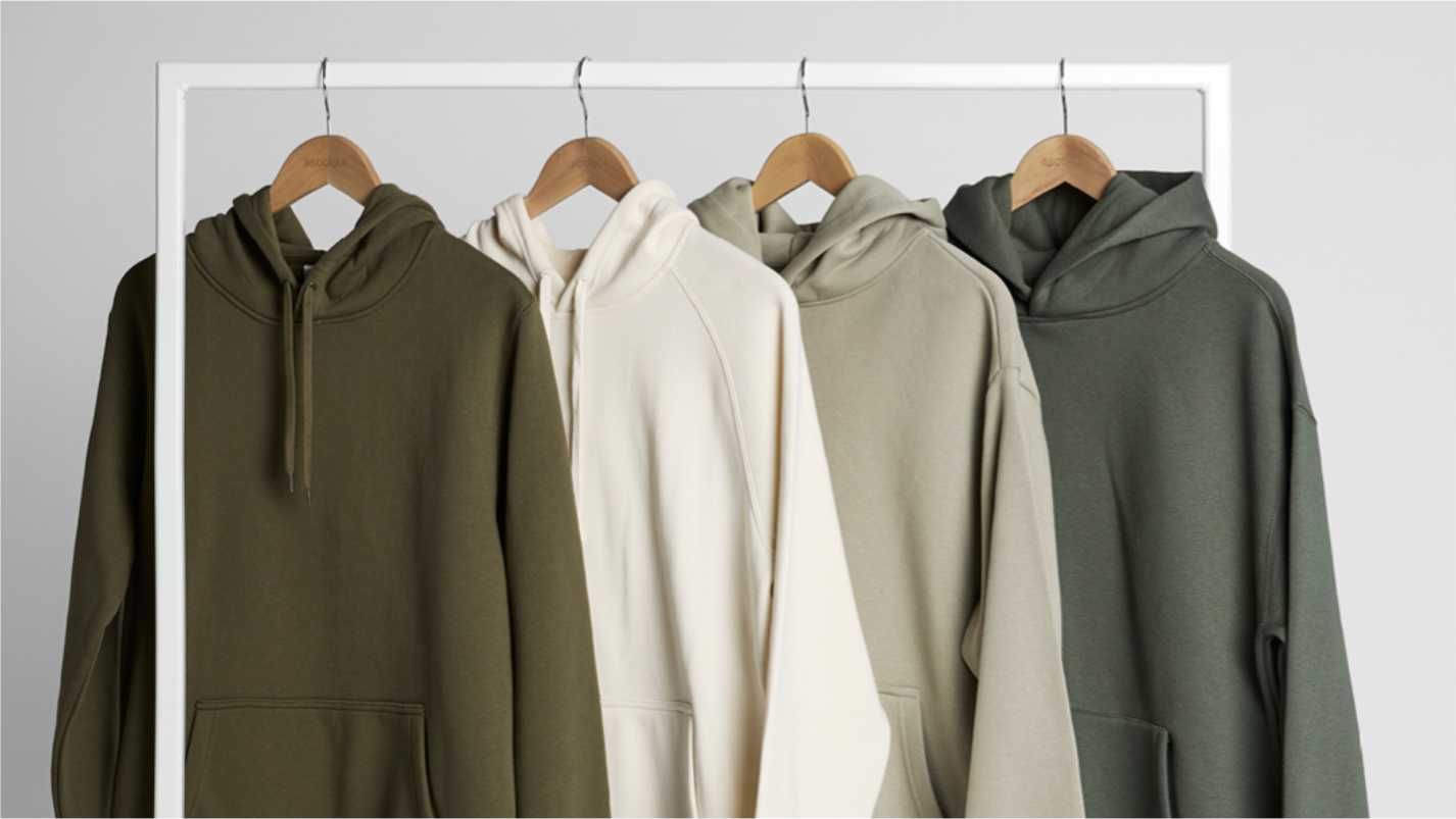 Neutral tone hoodies hanging on wooden hangers against a light background.