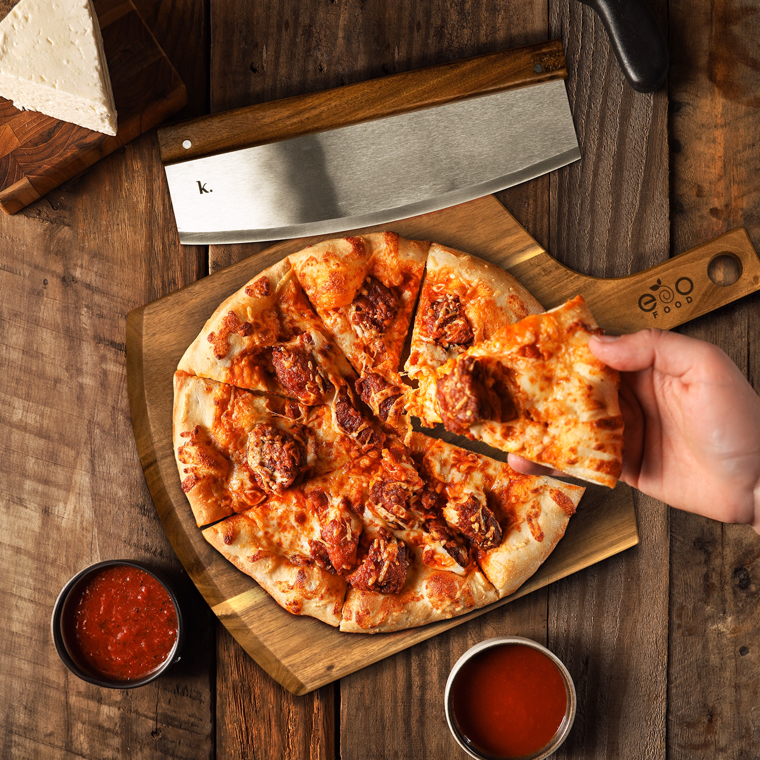 Wooden pizza board with fresh pizza, stainless steel cutter, and branded handle displayed on rustic table.