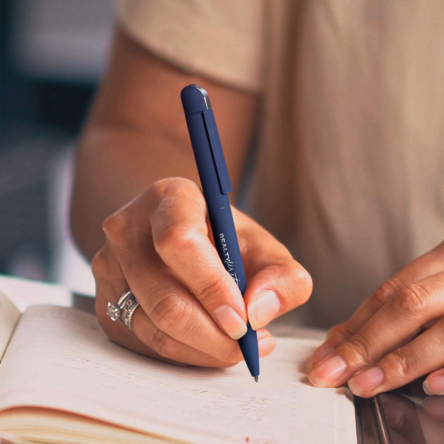 Person writing in notebook with navy metal pen engraved with logo.