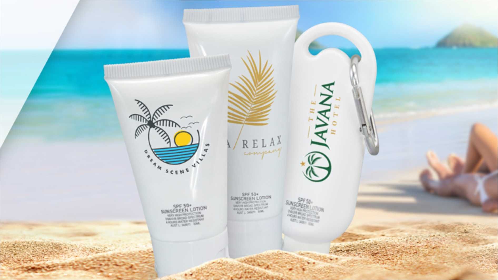 Branded sunscreen tubes on sandy beach with ocean background.