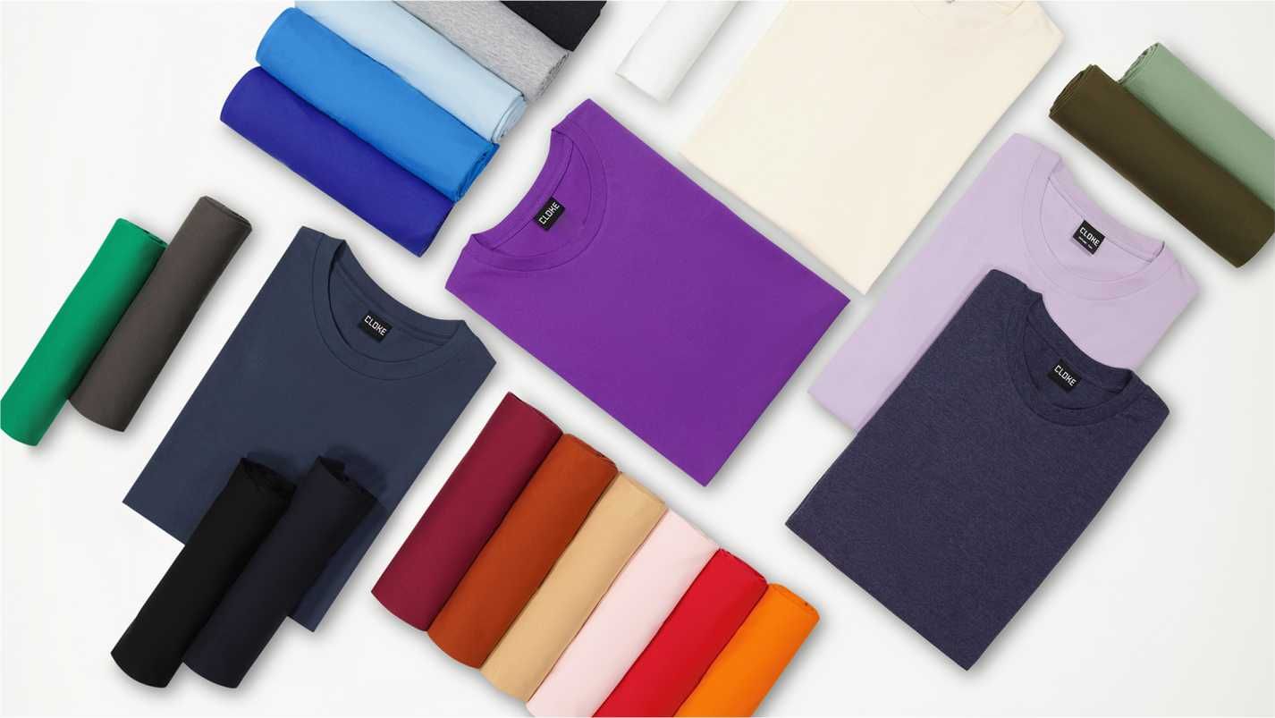Folded and rolled colourful T-shirts arranged neatly on a flat surface.