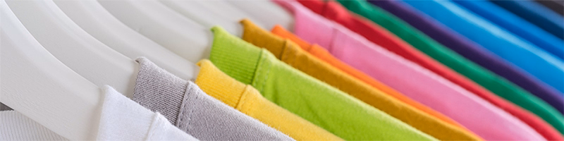 Close-up of assorted cotton T-shirts on hangers arranged by colour from white to blue