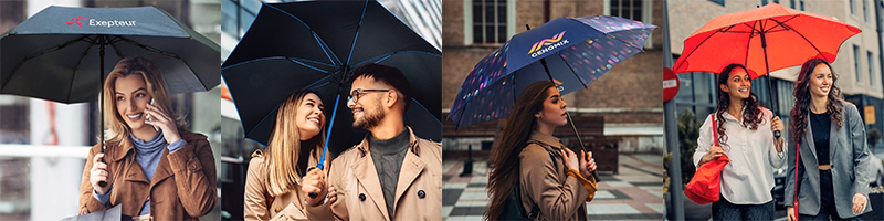 People walking outdoors holding assorted promotional umbrellas in black, patterned, and red colours with printed logos